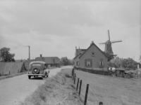 80 Olst: Opname van een auto die over de Rijksweg Zwolle-Deventer rijdt, met huizen en een molen (de Bökkers Mölle uit ...