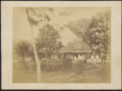 5096 -0001 Indonesische werknemers poseren voor een woonhuis met tuin en rieten dak van (waarschijnlijk) de ...