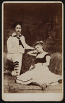 43 -111 Portret van twee vrouwen waarvan een verkleed als matroos, bij een hooibaal., 1877-01-01