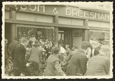 527 Verzamelde menigte met fiets voor de Vroom & Dreesman; man met megafoon, 1920-01-01