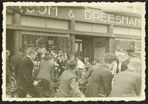 527 Verzamelde menigte met fiets voor de Vroom & Dreesman; man met megafoon, 1920-01-01