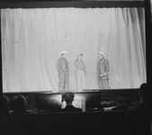 1327 Toneelvoorstelling: scene met drie acteurs waarvan 1 met sabel. Het doek is dicht en de orkestbak met pianist is ...