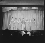1328 Toneelvoorstelling: 7 dames klaar voor de buiging op het toneel. Het doek is dicht, de pianist is zichtbaar in de ...