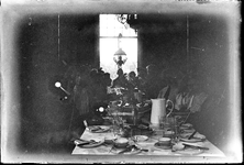 103 Gedekte eettafel binnenshuis met zittend gezelschap. Zeer donkere opname., 1910-01-01