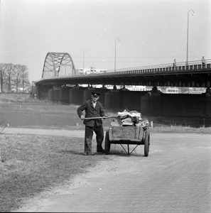506 Met een handkarretje wordt het afval opgehaald aan de Bolwerksweg. Op de achtergrond de Wilhelminabrug., 1961-01-01