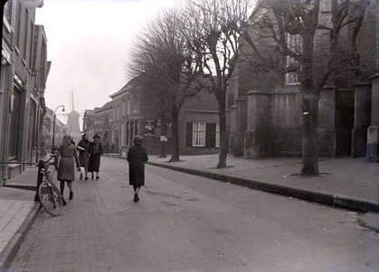 114 Wijhe: Opname van een straat in het dorp met voetgangers, een gedeelte van een kerk in beeld en een molen op de ...