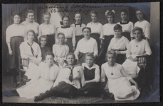 1033 Tien vrouwen, leerlingen en lerares aan de Vrouwenarbeidschool, afdeling Kostuumnaaien, poseren. Afgedrukt als ...
